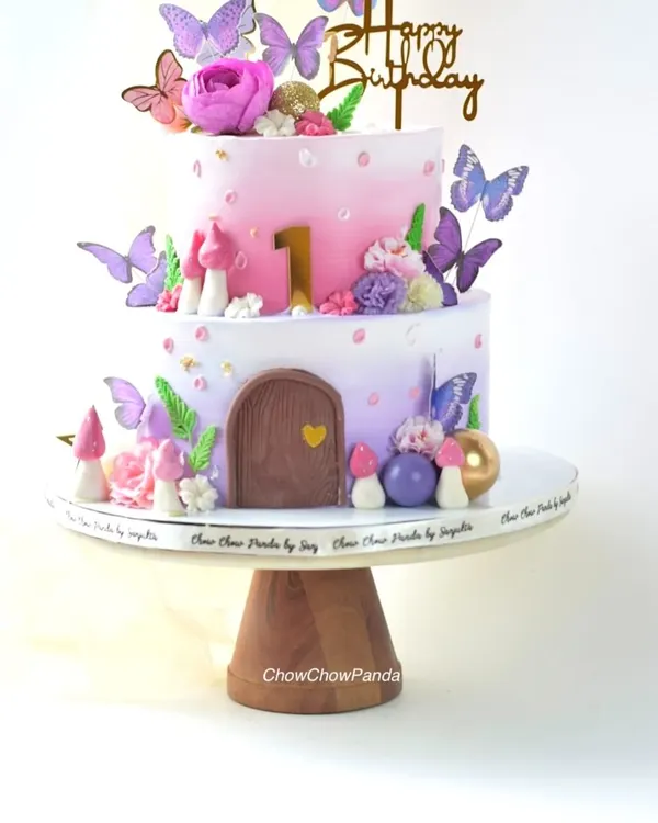 A closer look at the two-tier fairy house cake, showing the details of the edible mushrooms, flowers, and the number '1' for a first birthday.