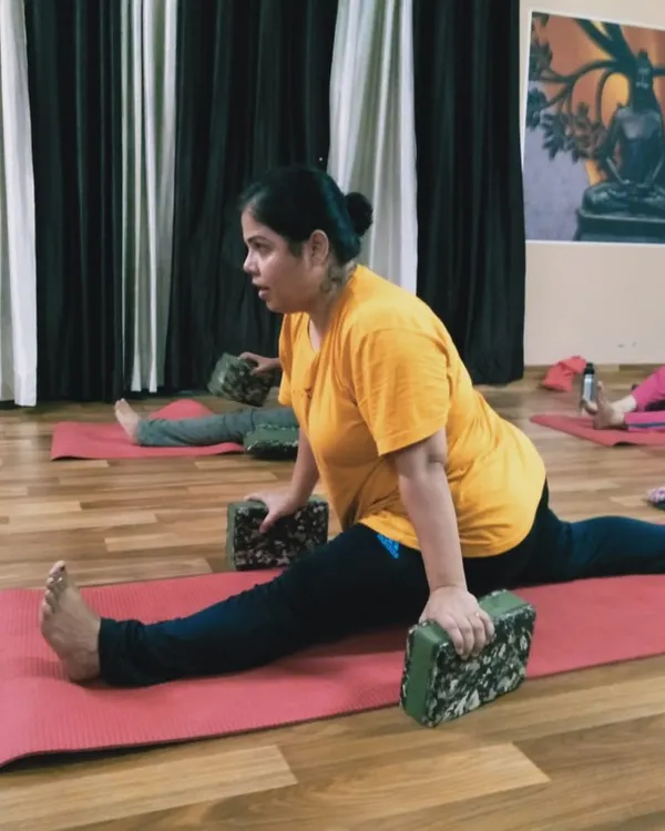 A student works on Hanumanasana (the splits) using yoga blocks for support. Props are essential in yoga therapy to help the body open up gradually and prevent injury.