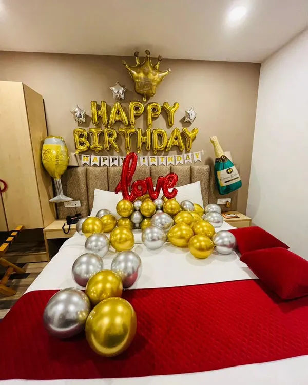 A classic romantic birthday bedroom setup. This decoration includes "Happy Birthday" foil balloons, a foil crown, and gold and silver balloons on the bed.