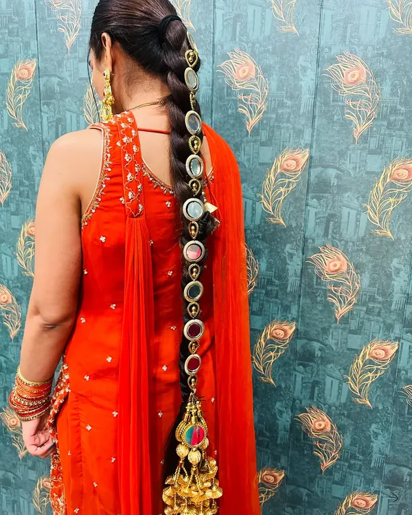 A close-up of a traditional Punjabi parandi (hair accessory) with mirror work and a large golden tassel. This is perfect for adding a folk touch to your Mehendi or Sangeet look.