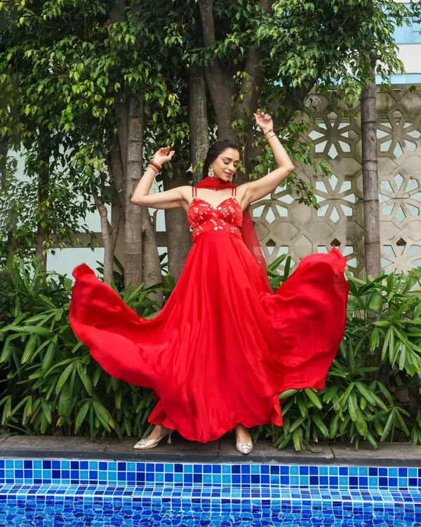 A vibrant and energetic shot from a styled photoshoot. The flowing red anarkali is paired with elegant makeup that is perfect for a Sangeet or reception.