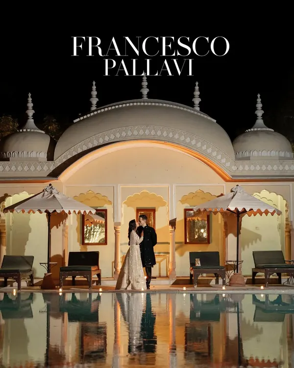 A stunning nighttime portrait of a couple at a palace, their figures reflected in the poolside. This wide shot establishes a scene of pure luxury and romance, perfect for a destination pre-wedding shoot.