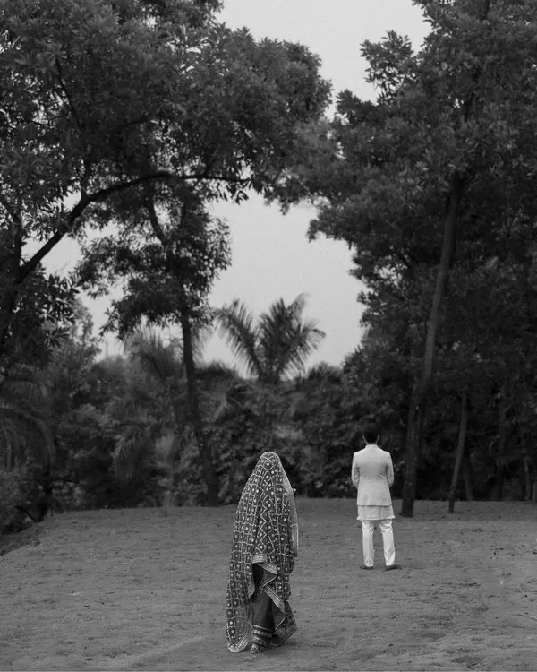 An artistic black and white shot of the bride and groom during their ceremony. The composition creates a sense of journey and togetherness as they walk through a natural landscape.