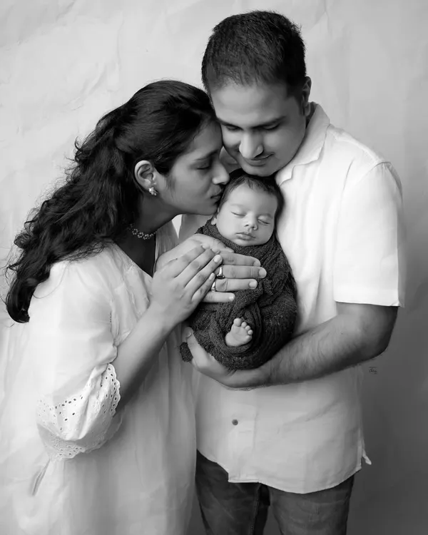 A truly timeless black and white family portrait. The lack of color emphasizes the tender emotions as a mother kisses her newborn, held securely in his father's arms.