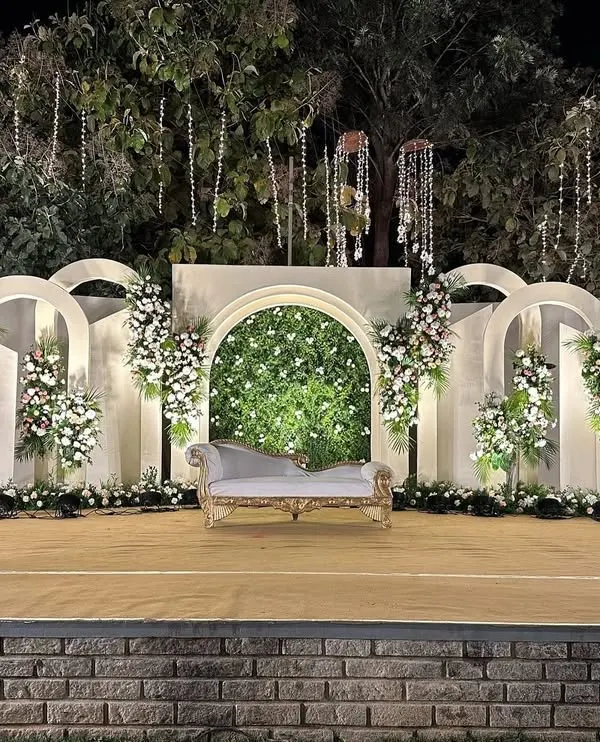 A perfect example of modern elegance. This outdoor stage features a series of clean white arches, a central greenery wall, and asymmetrical floral placements for a look that is both minimal and impactful.