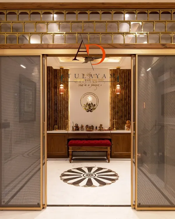 This grand pooja room entrance features sliding glass doors with a fine mesh and a transom with brass and glass detailing. The design creates an inviting yet separate sacred space, with a view of the beautiful marble floor inlay inside.