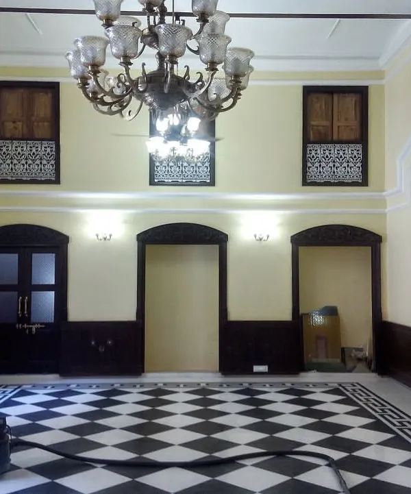 The main hall of a 19th-century haveli after restoration, featuring a classic checkerboard marble floor, restored doors, and a magnificent heritage chandelier, ready for its new life.