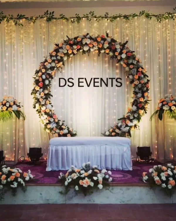 A beautiful and elegant circular floral arch for an indoor reception. This design uses peach and white roses against a backdrop of fairy lights, creating a warm and inviting focal point for the couple's seating.