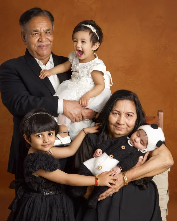 The pure, unscripted joy of three generations together. This portrait captures the grandparents' pride, the siblings' excitement, and the peaceful sleep of the newest family member.