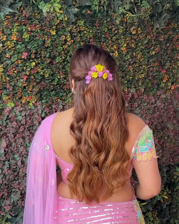 A back view of this dreamy floral half-updo. The combination of soft waves and a colorful floral clip makes this the perfect hairstyle for a fun and vibrant Mehendi party.