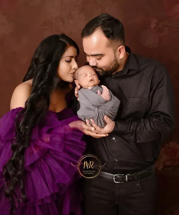 A tender moment as new parents admire their newborn baby. The dark, moody background helps to focus all the attention on the family's loving bond.
