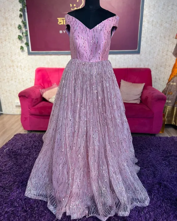 A full view of a beautiful lilac-pink sequin gown on a mannequin. This off-shoulder ball gown is perfect for receptions and evening parties.