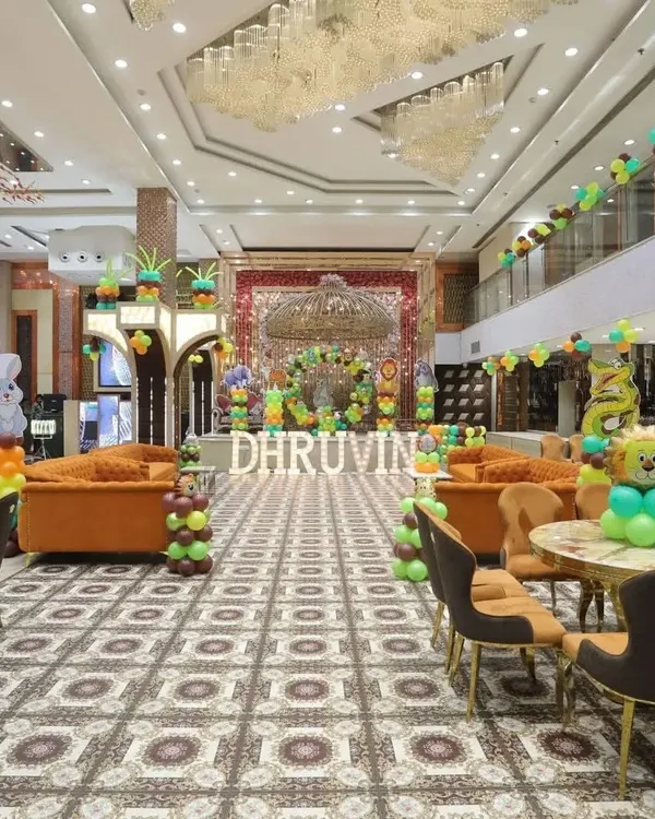 A wide-angle view of a large-scale jungle-themed decoration in a banquet hall. The setup includes a central stage backdrop, marquee letters, and balloon decorations throughout the venue.