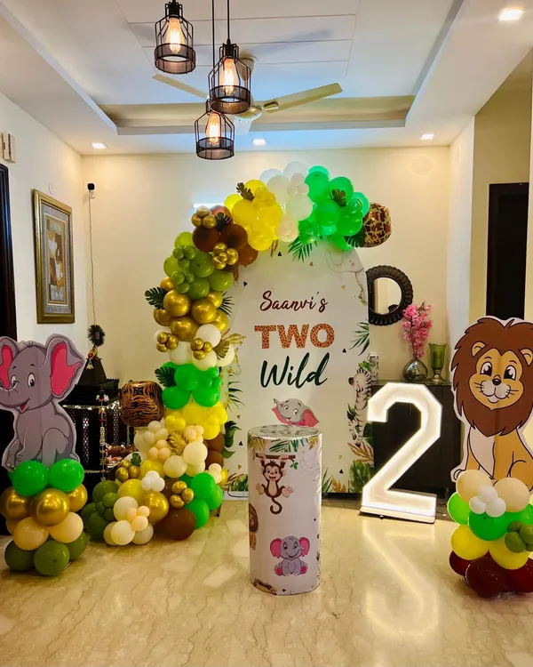 A 'Two Wild' jungle safari theme for a second birthday, set up in a spacious living room. This decor features an arched backdrop, marquee number '2', and cutouts of a lion and elephant.