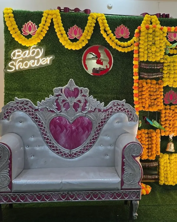A stunning traditional baby shower backdrop. This design features a checkerboard of yellow and orange marigolds on a grass wall, a modern neon sign, and an elegant throne for the mom-to-be.