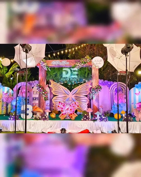 A breathtaking enchanted garden setup for Hithartha's first birthday. This outdoor night event features a massive stage with a giant butterfly centerpiece, mushroom props, and beautiful lighting that creates a truly magical atmosphere.