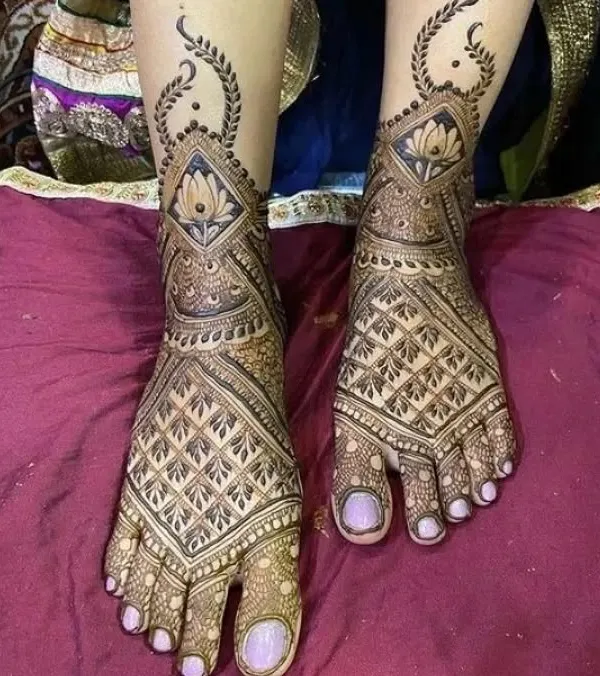 An elegant foot mehendi design featuring a central lotus in a diamond-shaped frame. The pattern extends gracefully up the foot, perfect for showing off with your bridal footwear.