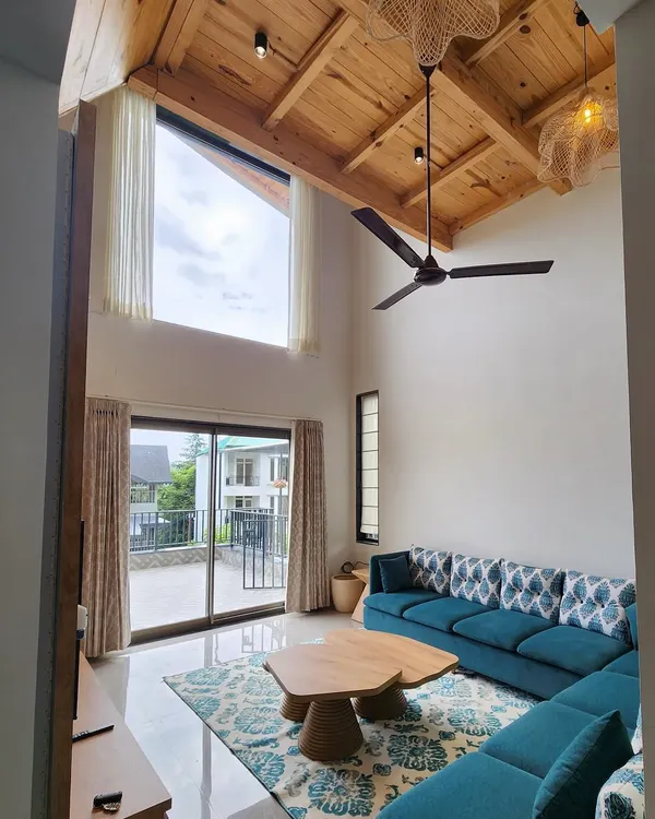 For this beautiful villa in the hills, we designed a living space that feels open and connected to nature. The double height room features a vaulted wooden ceiling, a large teal sectional sofa, and our custom-made wooden coffee table, creating a perfect blend of comfort and rustic charm.