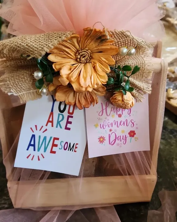 This is a close-up of a hamper I designed for Women's Day. It features a wooden crate base, soft pink tulle wrapping, and a rustic burlap and flower detail, complete with encouraging "You Are Awesome" and "Happy Women's Day" cards.