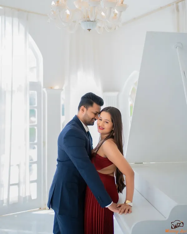 An elegant and romantic pre-wedding photo of Jui and Vaikrant. The all-white room with a grand piano provides a classic and sophisticated backdrop for their portrait.