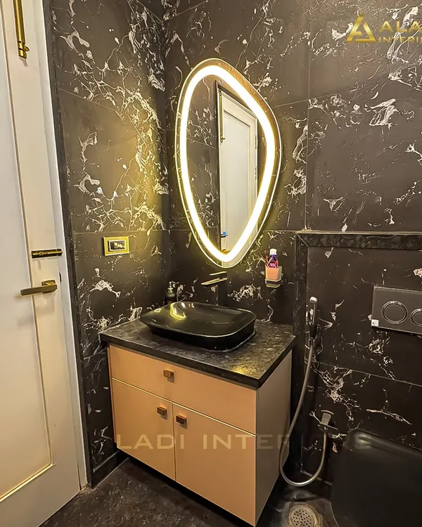 A dramatic bathroom design featuring black marble-patterned tiles and a uniquely shaped backlit mirror. The minimalist vanity and black vessel sink add to the modern, luxurious feel.