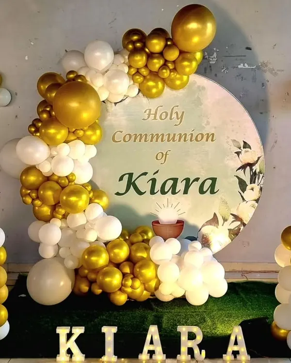 An elegant decoration for a Holy Communion ceremony. This setup features a custom circular backdrop, a white and gold balloon garland, and marquee letters with the child's name.