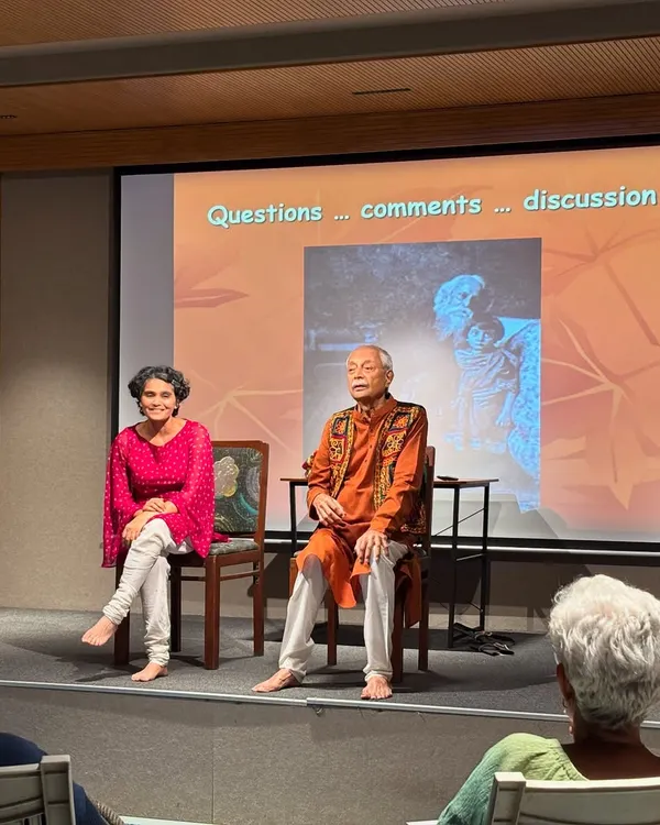 A candid shot of a speaker and presenter on stage during a discussion, with the audience visible.