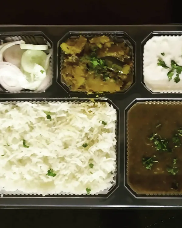 A complete vegetarian thali packed and ready to go. This meal includes dal, a dry vegetable, raita, salad, and rice, offering a balanced and satisfying lunch or dinner.