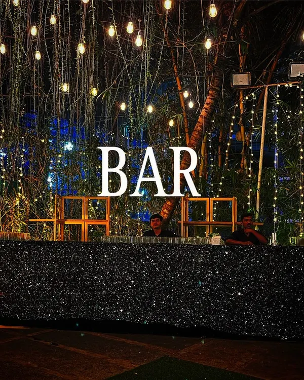 A black sequin bar creates a stunning, glamorous look for any evening event. Topped with a bold "BAR" marquee sign and set under a canopy of string lights, this setup is designed to impress.