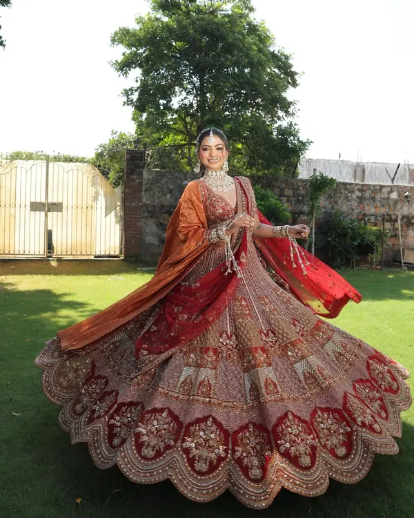 This is the hero shot. A full, breathtaking twirl in a magnificent red and orange bridal lehenga, showcasing the royal flare and intricate craftsmanship that makes a bride's dream come true.