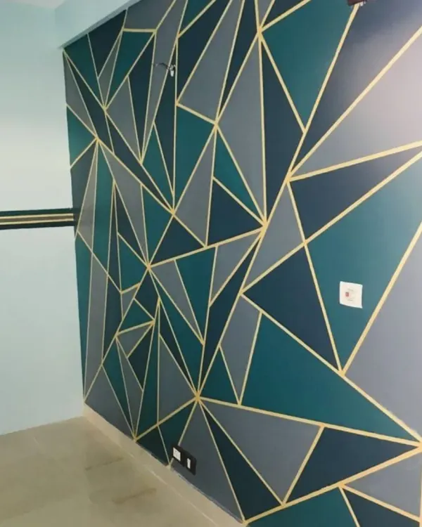 A bold geometric accent wall featuring a pattern of interlocking triangles in shades of teal, grey, and black, defined by crisp gold lines for a modern and luxurious finish.