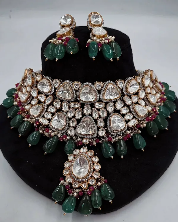 A stunning Polki necklace set with large, uncut triangular stones and emerald green bead drops, displayed on a bust.