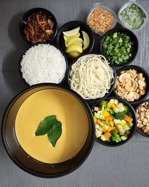 This is my signature Khao Suey DIY meal kit. I deliver the rich coconut curry, noodles, and a variety of fresh toppings like fried garlic, spring onions, and cashews all packed separately. It allows your guests to customize their own perfect bowl.