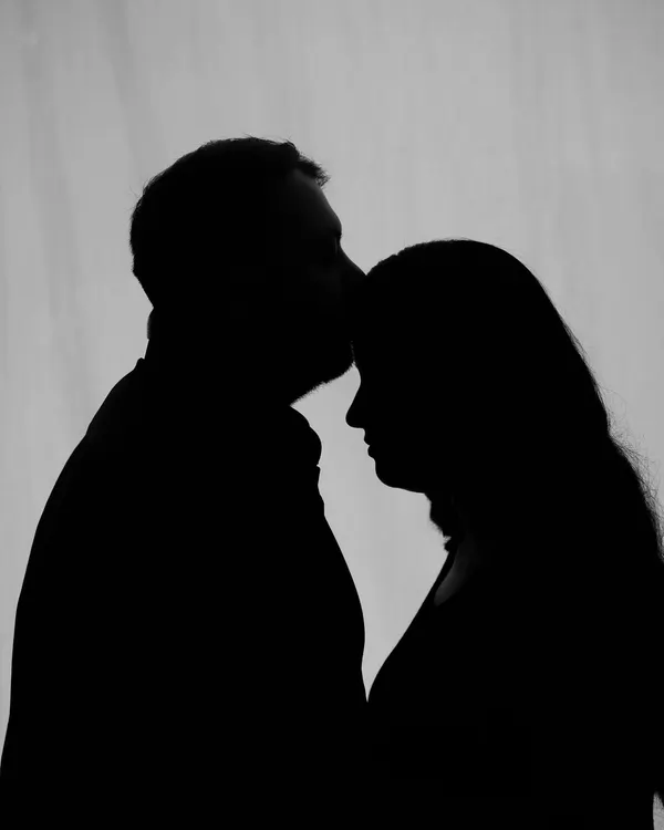An intimate silhouette of a partner kissing the mom-to-be's forehead. This style creates a timeless and emotional image, focusing purely on the shape and connection.