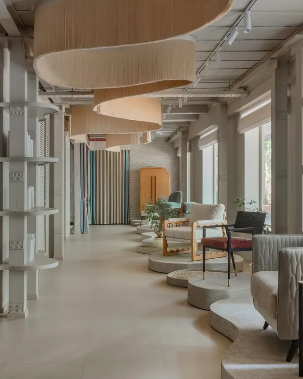 The core concept for the JOSMO showroom was to create a fluid, gallery-like experience. This wide view shows how the undulating ceiling fringe and curved floor plinths guide movement, creating distinct vignettes for furniture display without the use of traditional walls.