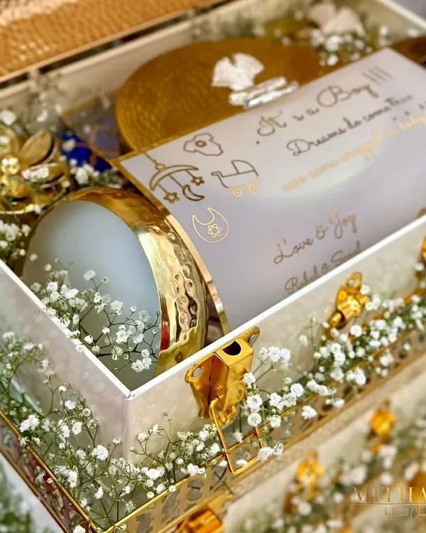 A close-up of a birth announcement hamper for a baby boy. It includes a personalized card that reads "It's a Boy! Dreams do come true," nestled among treats in elegant gold and white packaging.