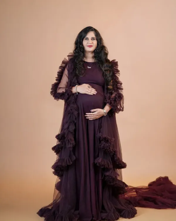 A full-length portrait showcasing a dramatic, dark purple ruffled maternity gown against a neutral studio backdrop. This look is perfect for creating an elegant and high-fashion feel for your pregnancy photos.