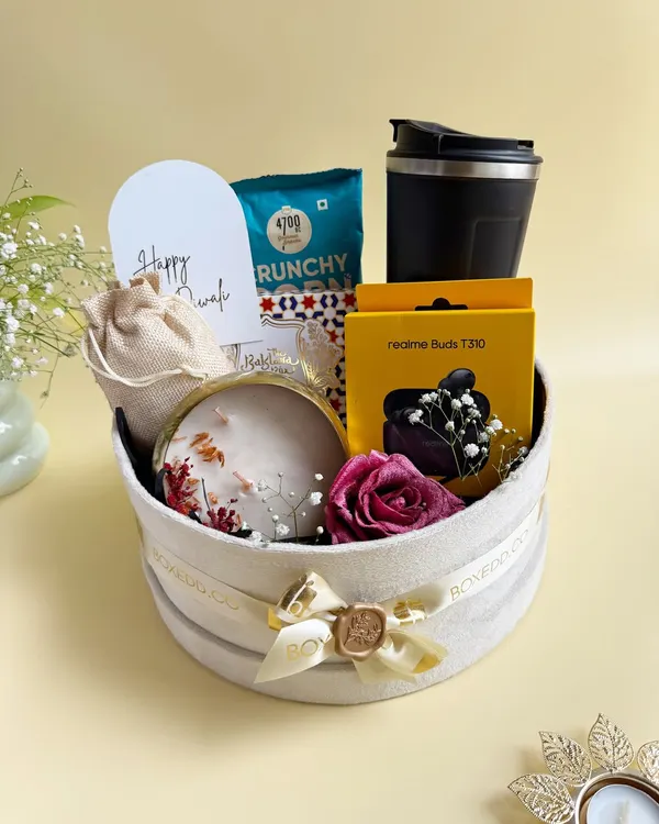 A luxurious Diwali hamper featuring a mix of modern tech and traditional treats. It includes Realme Buds, a travel tumbler, gourmet snacks, and a decorative candle.