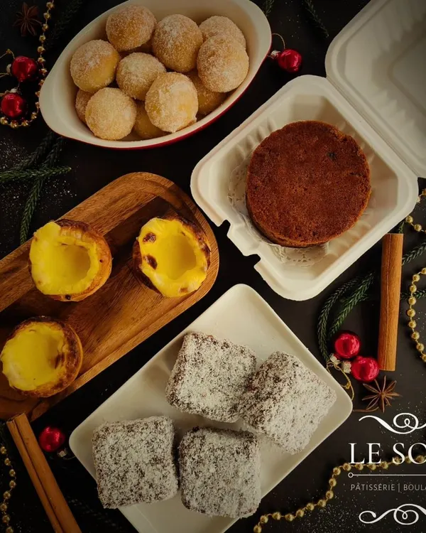 A festive flatlay of my Christmas 2024 menu. This spread includes eggless treats like Portuguese Pastel de Nata, Australian Lamingtons, mini fruit cakes, and doughnuts.
