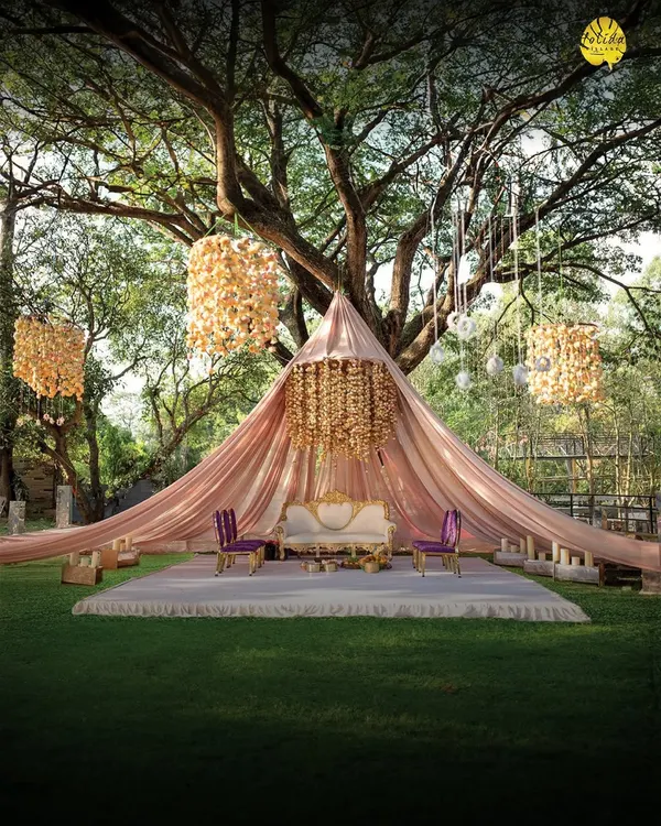 Welcome to Holiday Village, where we turn your dream events into reality. This stunning mandap, set under the canopy of a majestic tree, is just one of the many magical settings we can create for your special day.