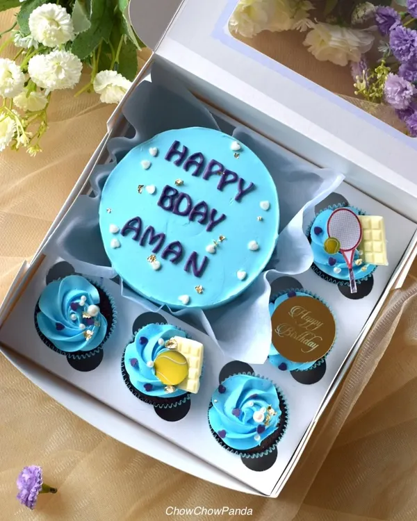 A tennis-themed bento box I made for a birthday. The set features a light blue mini cake and matching cupcakes decorated with edible tennis balls, rackets, and white chocolate bars.