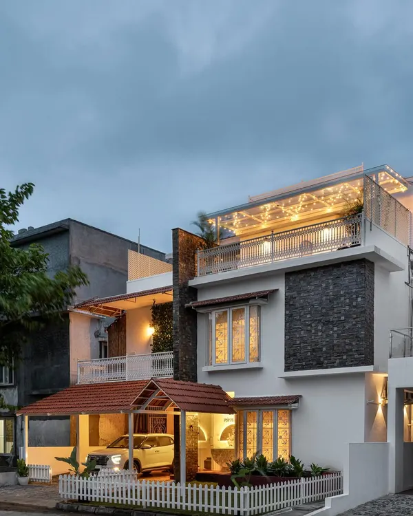 The exterior of 'Mina Nivas' is a beautiful blend of styles. The stone cladding, traditional sloping roof, and white picket fence create a charming and inviting facade that hints at the colonial-inspired interiors within.