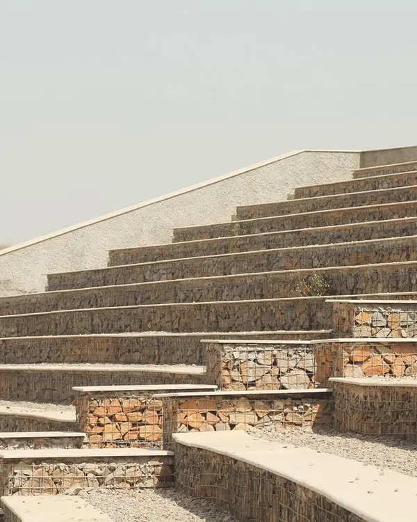 The stepped seating of the Aravali Biodiversity Park Amphitheatre is constructed with gabion walls, which are wire mesh cages filled with stones sourced directly from the site. This sustainable technique minimizes waste and ensures the structure is visually integrated with the landscape.