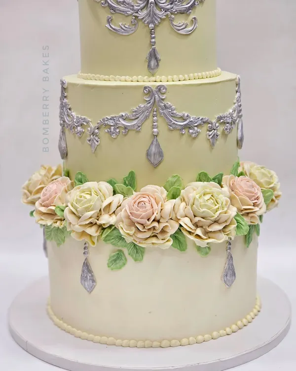 An elegant three-tiered engagement cake decorated entirely with buttercream. The focus is on the hand-piped pastel roses and delicate silver scrollwork, techniques I cover in my advanced buttercream class.