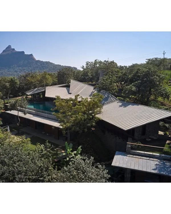 An elevated view of the Lateral Verandah House, nestled within the lush landscape of Lonavala. The structure's fragmented form is a deliberate strategy to minimize its impact on the site and maximize its engagement with the natural environment and distant views.