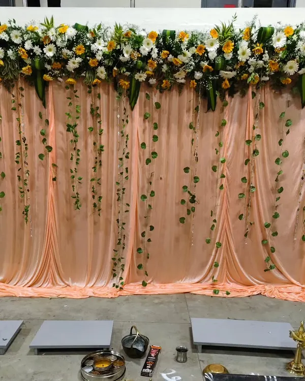 A simple and elegant backdrop for a 25th-anniversary celebration, featuring a peach-colored curtain, a floral topiary, and hanging green vines.