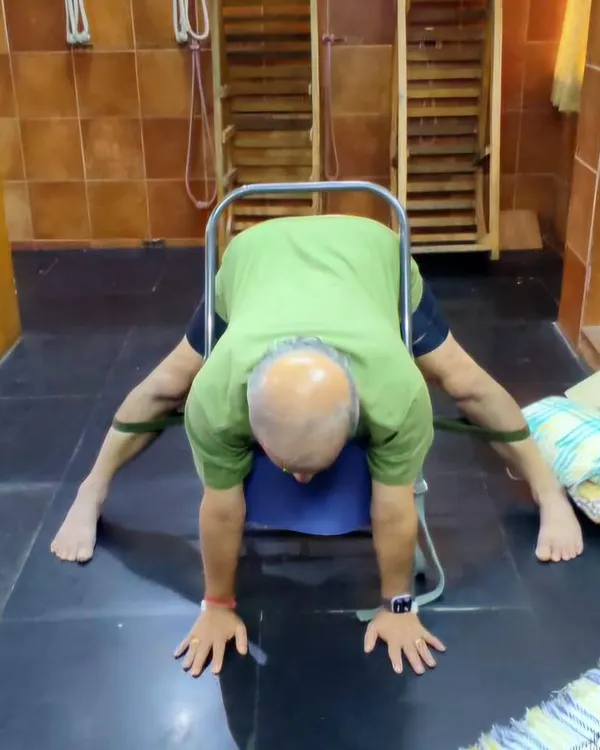 A wide-legged forward bend using a chair for support.