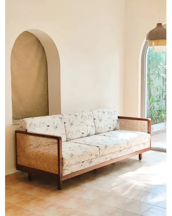 The Gubbi Sofa, a perfect blend of solid teak wood, natural rattan, and customizable floral fabric. Its clean lines and natural materials make it a versatile and elegant centerpiece for any living room.
