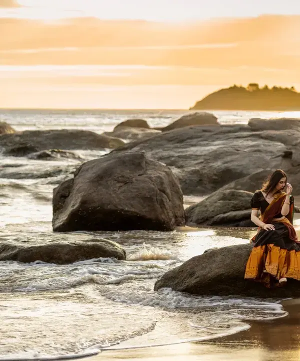 A breathtaking sunset at a rocky beach in Mangalore provides the perfect canvas for a dramatic and romantic pre-wedding portrait.