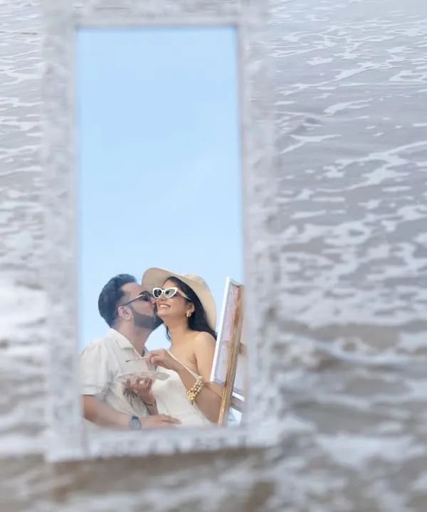 A creative and romantic kiss reflected in a mirror placed on the beach. This artistic shot from a Goa pre-wedding shoot is unique and memorable.